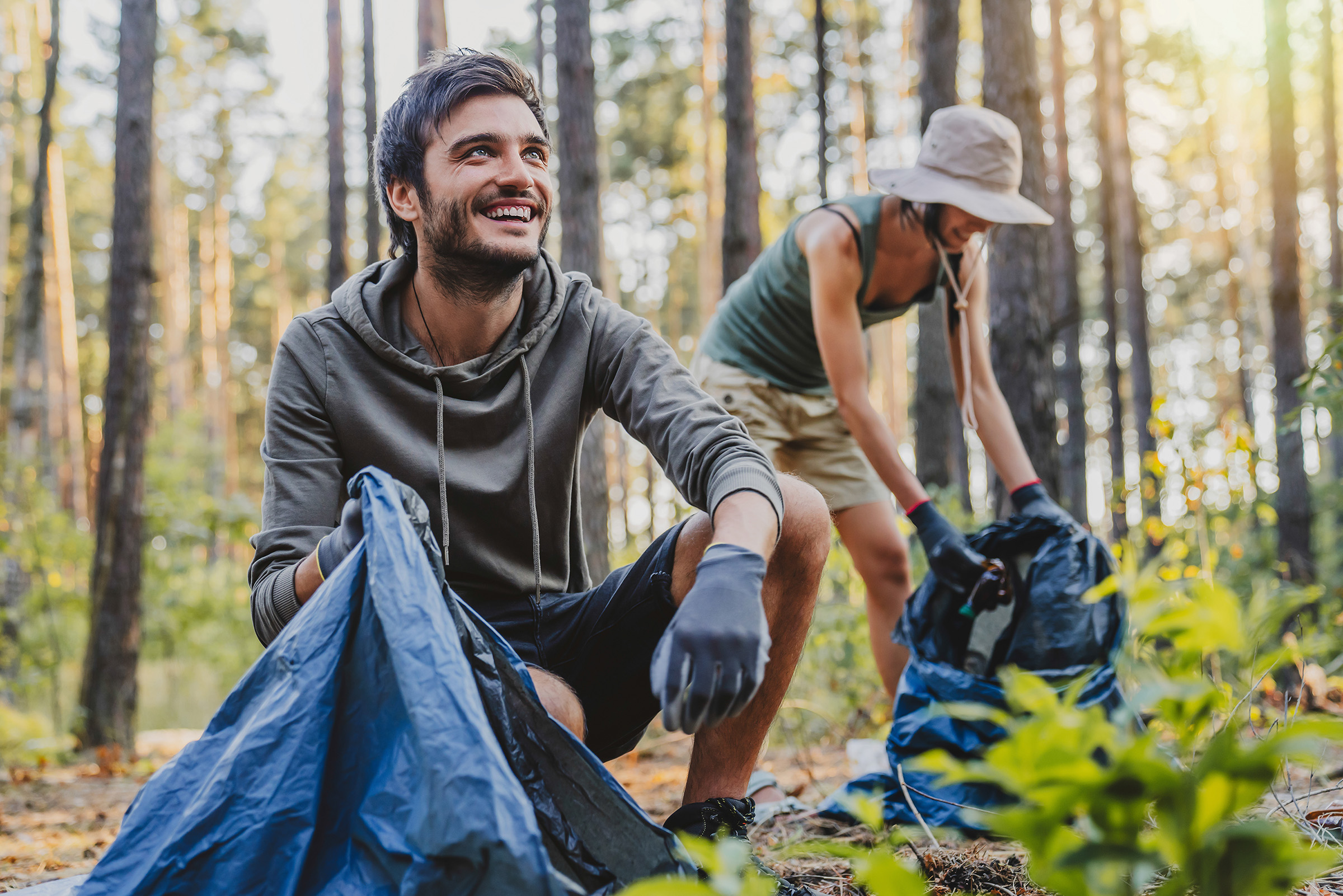 Cheerful man looking away while collecting trash with friends in a national park